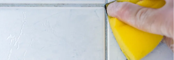 Hand reinigt Fliesenfugen mit Schwamm